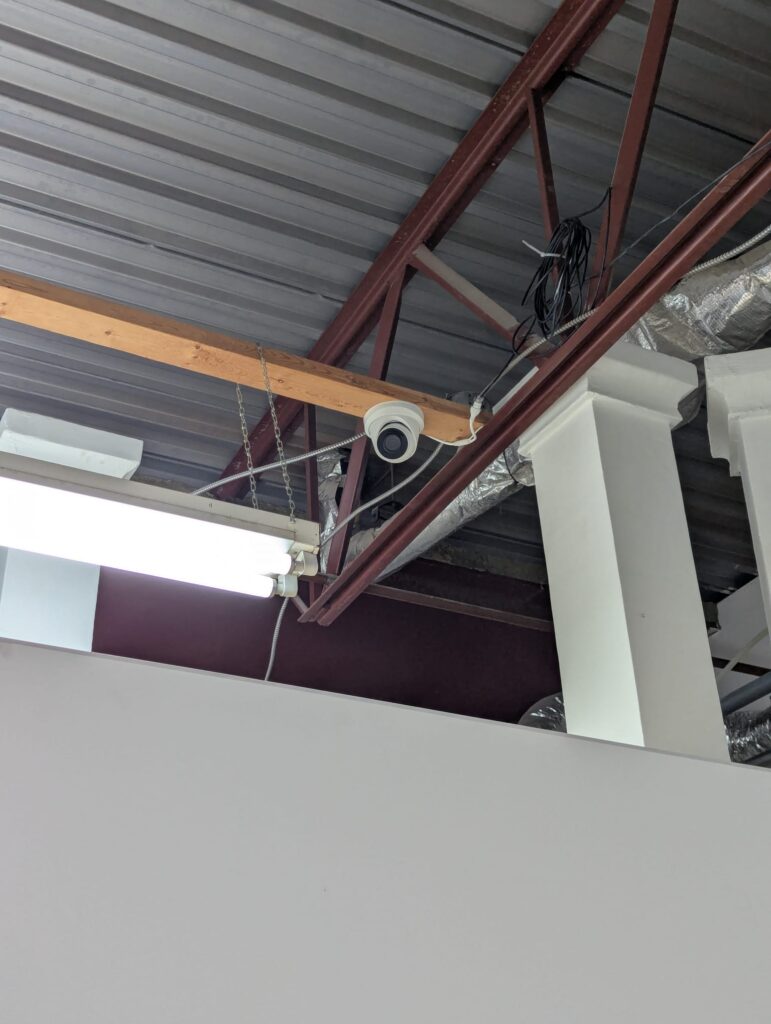 Security camera mounted to a warehouse ceiling structure